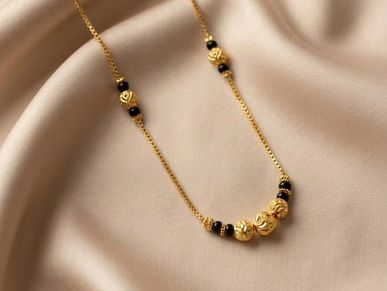 Elegant gold chain necklace with black beads on a soft beige fabric.