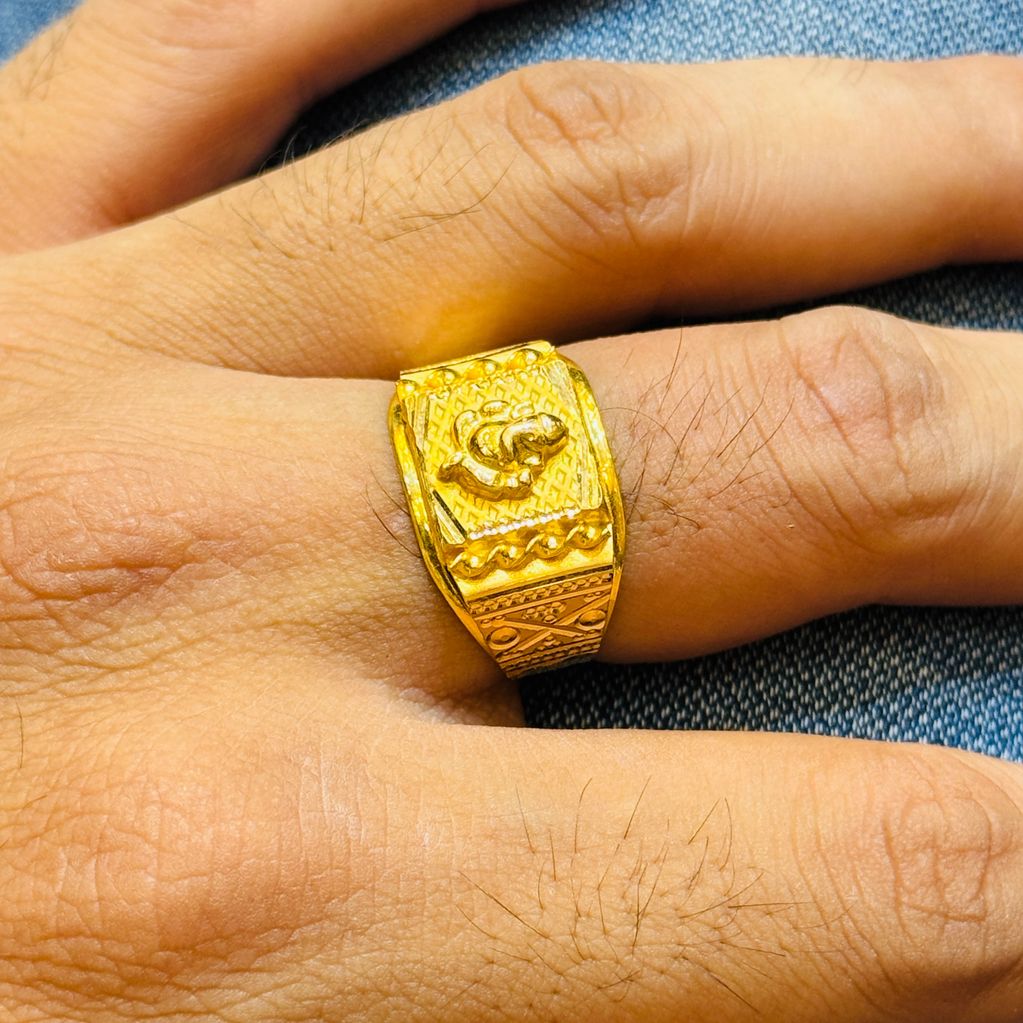 A gold ring with intricate designs worn on a finger.