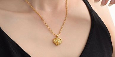 Gold heart-shaped pendant necklace on a person wearing a black top.