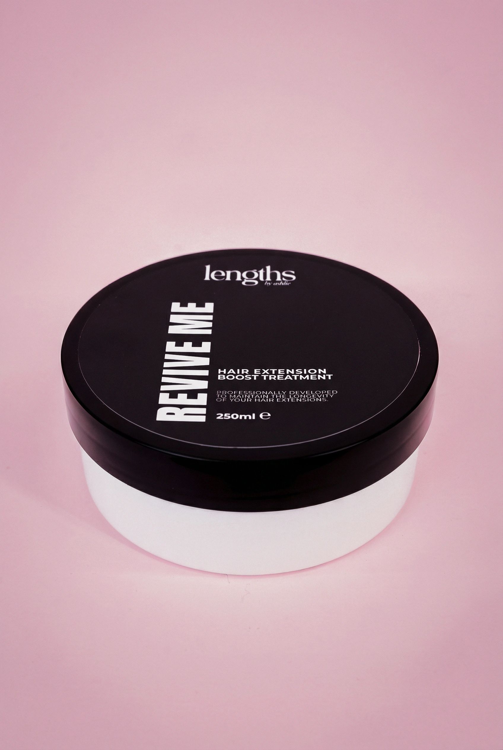 A container of REVIVE ME hair extension boost treatment by lengths on a pink background