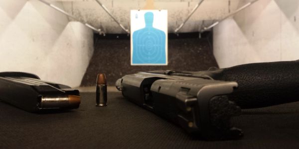Handgun, magazine, and bullet at an indoor shooting range with a target.
