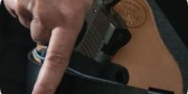 Hand gripping a handgun in a leather holster.