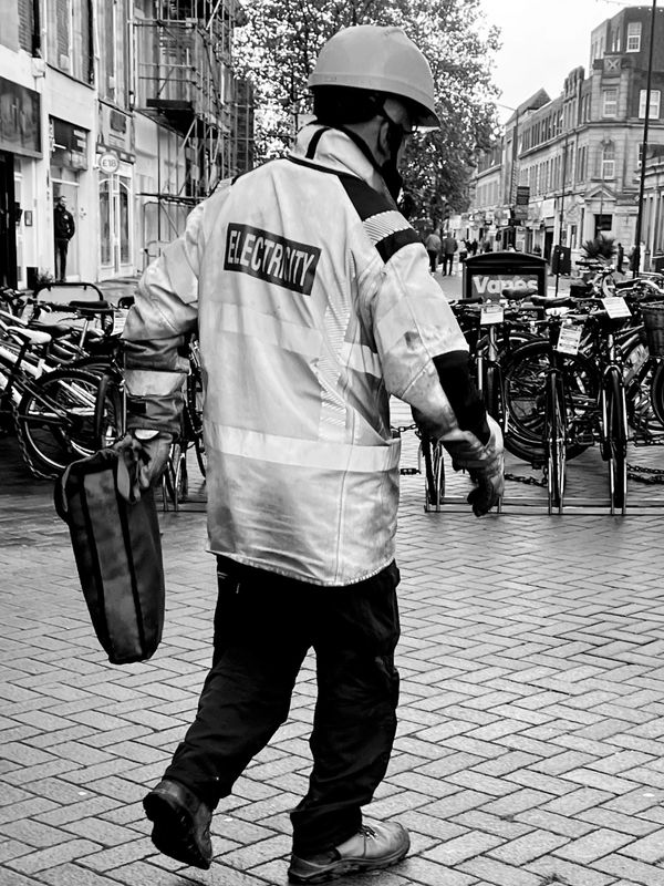 Electric man 
image of a ground worker  black and white high vis jacket walking towards some bikes 