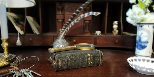 Vintage book, magnifying glass, and keys on a wooden desk.