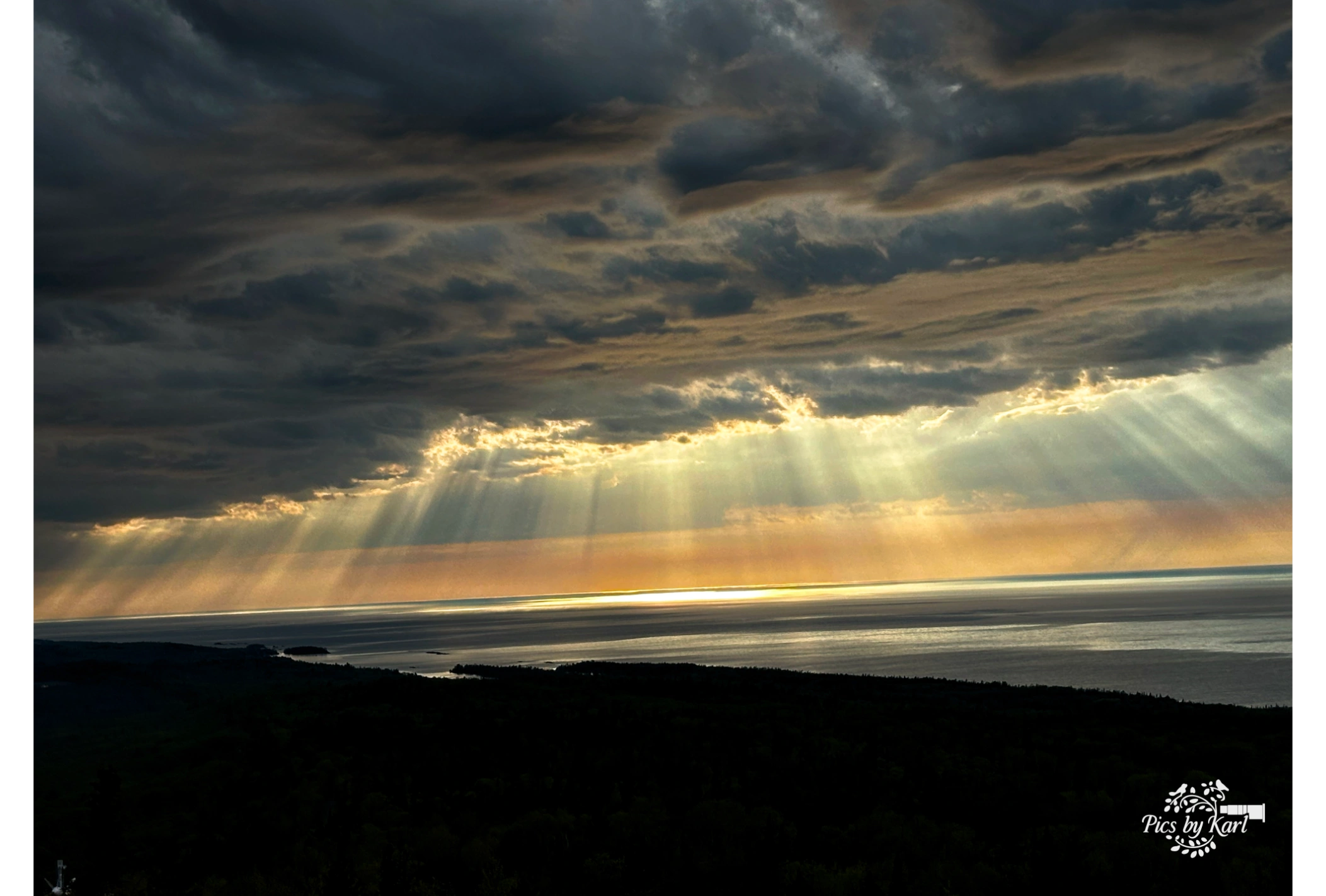 Sun rays breaking through dark clouds over a sea view.