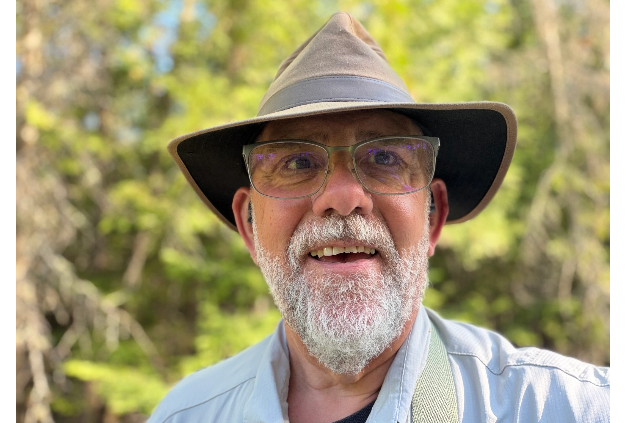 Smiling older man with glasses and a hat outdoors.