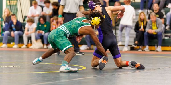 Two wrestlers in action on a wrestling mat with spectators in the background.