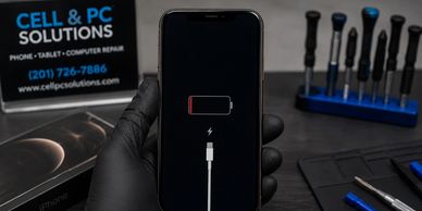 Gloved hand holding a low battery iPhone in a repair shop setting.