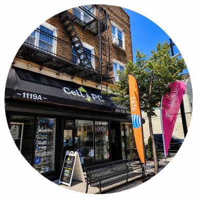 Exterior of a cell phone and PC repair shop with promotional flags and a bench outside.