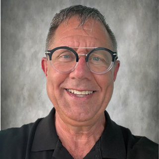 Smiling man with glasses in a black shirt against a gray background.
