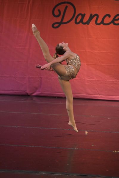 A dancer performs an elegant leap with a raised leg on stage.