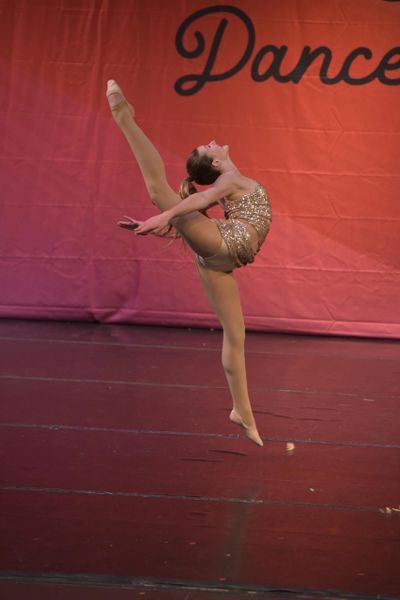 A dancer performs an elegant leap with a raised leg on stage.