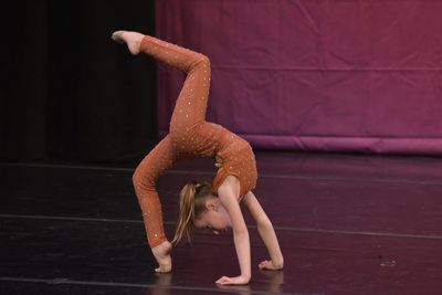 Young girl performing an acrobatic handstand on stage.