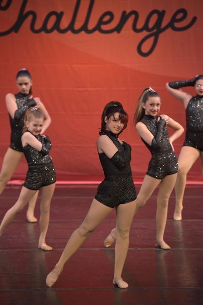 Young dancers in black costumes perform on stage during a dance challenge.