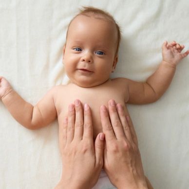 smiling baby receives abdominal massage from mother