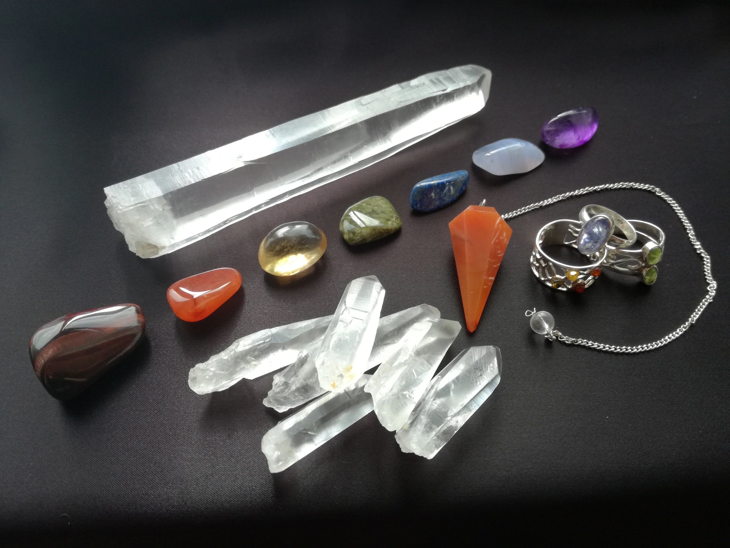 A collection of assorted crystals, gemstones, and silver rings on a black surface.