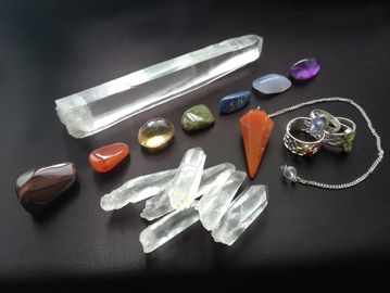 A collection of crystals including quartz points, tumblestones, a pendulum and rings