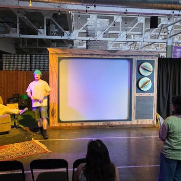 A man stands near a large TV screen setup in a warehouse-style room.