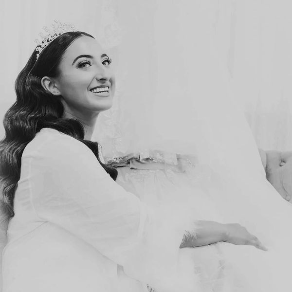 Bride smiling brightly, wearing a tiara and a soft, fluffy robe.