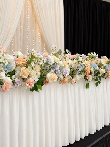 Elegant floral arrangement on a white draped table with soft pastel roses and greenery.