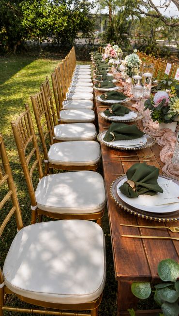 Elegant outdoor dining setup with gold chairs and green napkins.