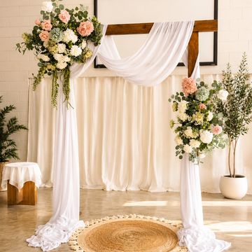 Elegant wedding arch draped with white fabric and floral arrangements.