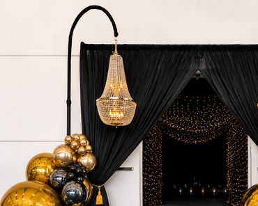 Elegant entrance with black curtains, golden balloons, and hanging chandeliers.