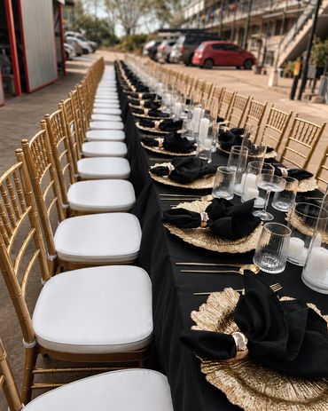 Elegant outdoor dining setup with gold chairs and black tablecloth.
