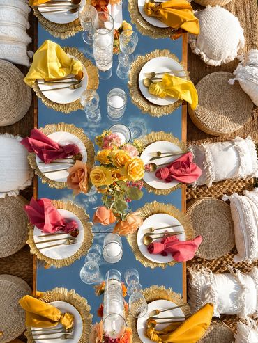 Elegant outdoor table setting with gold accents and colorful napkins on a reflective glass table.