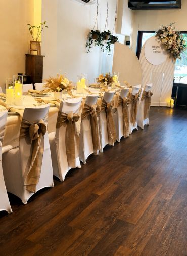Elegant dining setup with white chairs and gold ribbons in a cozy room.