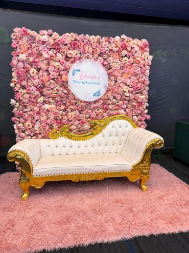 Elegant white and gold sofa in front of a pink floral backdrop for a wedding ceremony.