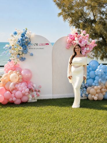 A woman in a white dress at a gender reveal party with pink and blue decorations.