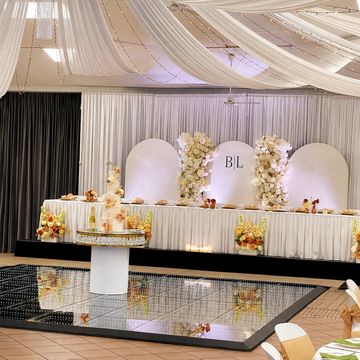 Elegant wedding reception with white drapes, floral arrangements, and a mirrored dance floor.