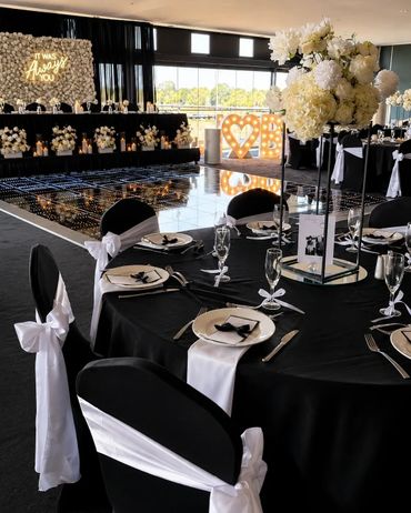 Elegant black and white wedding reception setup with floral centerpieces and illuminated love sign.