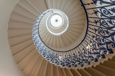 Looking up a spiral staircase with intricate blue railing and bright skylight.