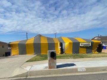 Large yellow and gray tent structure on a residential driveway under a blue sky.