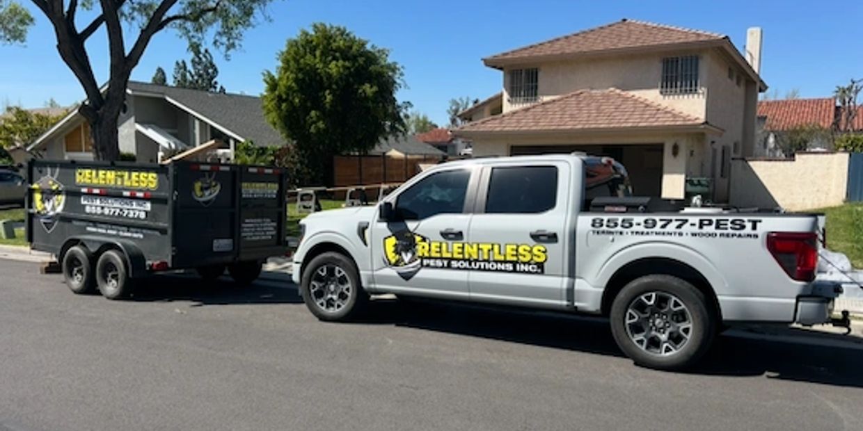 White truck and trailer with Relentless Pest Solutions branding parked on a residential street.