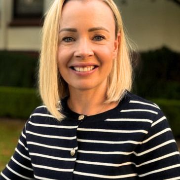 Smiling woman with blonde hair in a striped sweater outdoors.