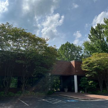 Office building surrounded by trees under a partly cloudy sky.