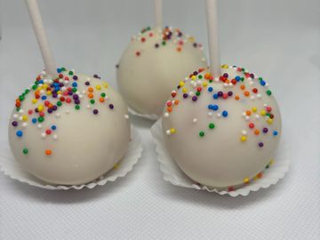 Three white chocolate cake pops with colorful sprinkles on white sticks.