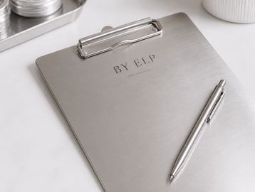 A sleek metal clipboard with a matching pen on a white surface.