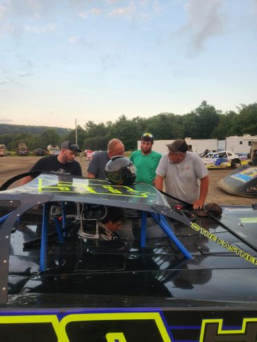Group discussing strategy around a race car with a driver inside.