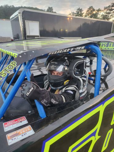 Racecar driver giving thumbs up inside a black and neon green racecar.