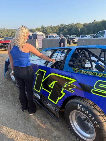 Woman in blue top standing beside a blue race car numbered 14Z.
