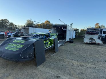 Race car number 58 with neon green decals parked near trailers.