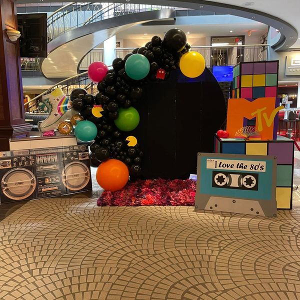 80s-themed photo setup with colorful balloons, cassette tape, MTV logo, and Rubik's cube.