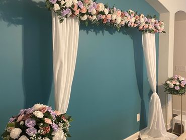 Floral wedding arch with white drapes against a teal wall.