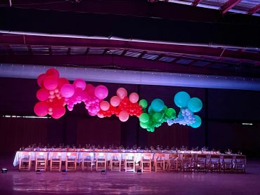 Colorful balloons above long dining tables in a dimly lit room.