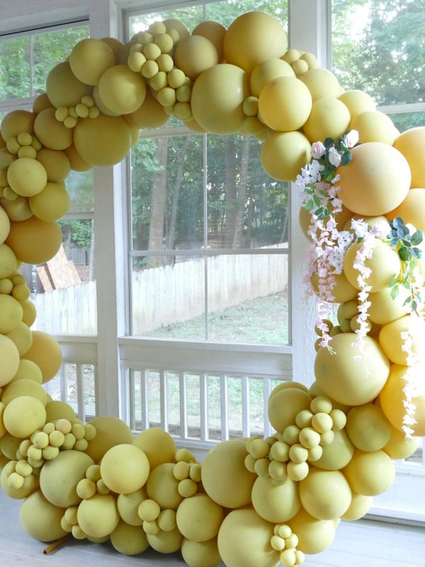 Large yellow balloon wreath with floral accents by a window.