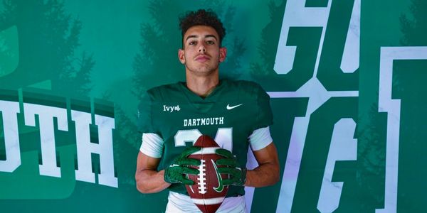 Football player in Dartmouth uniform holding a football against a green backdrop.